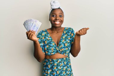 Kıllı türban takan genç Afrikalı bir kadın elinde 20 İsveç kronu banknotuyla gururla bağırıyor, zaferi ve başarıyı kutluyor. 