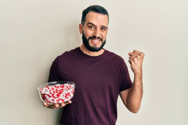 Sakallı genç adam elinde haplarla dolu bir kaseyle gururla bağırıyor zaferi ve başarıyı kutluyor. 