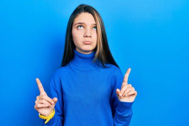 Boğazlı kazak giyen genç esmer kız üzgün ve üzgün görünüyor, parmaklarıyla yön gösteriyor, mutsuz ve depresif.. 