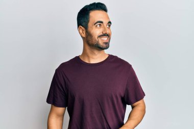 Latin kökenli genç bir adam günlük giysiler giyiyor, rahat bir görünüm takınıyor, doğal bir yüz ifadesi ve kendinden emin bir gülümsemeyle poz veriyor.. 