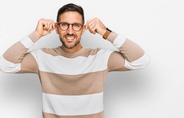 Sakallı, sıradan giyinen, gözlüklü, gülümseyen kulakları parmaklarıyla çeken yakışıklı bir adam. Komik bir jest. deneme sorunu 