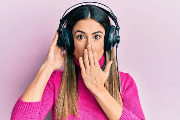 若いヒスパニック系の女性は 手で口をカバーヘッドフォンを使用して音楽を聞いてショックを受け 間違いを恐れている 驚きの表情 — ストック写真