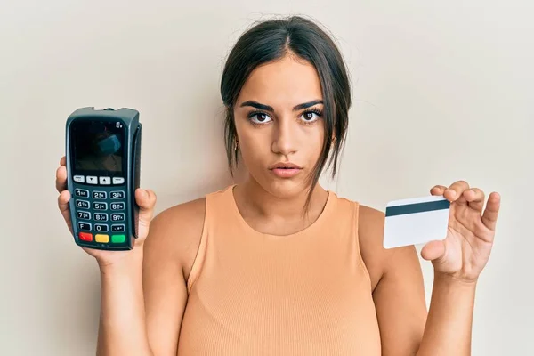 Młoda Brunetka Trzymająca Dataphone Kartę Kredytową Zrelaksowana Poważnym Wyrazem Twarzy — Zdjęcie stockowe