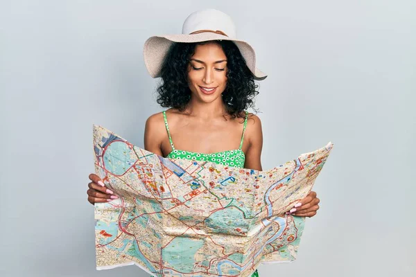 Young latin girl wearing summer hat holding city map smiling with a happy and cool smile on face. showing teeth.