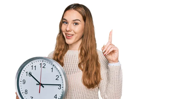 Mujer Rubia Joven Sosteniendo Gran Reloj Sorprendido Con Una Idea —  Fotos de Stock