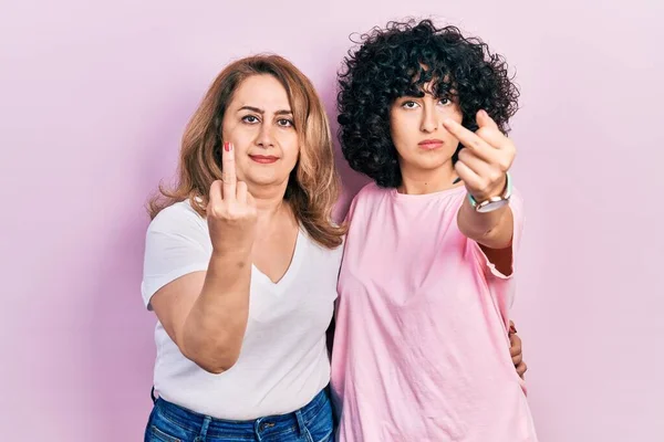 Middle east mother and daughter wearing casual clothes showing middle finger, impolite and rude fuck off expression