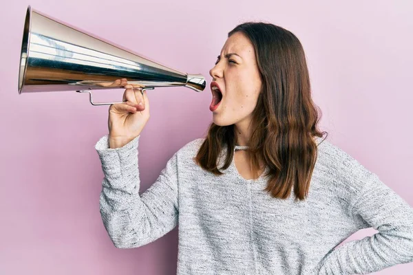 Young brunette woman shouting and screaming through vintage megaphone over pink isolated background