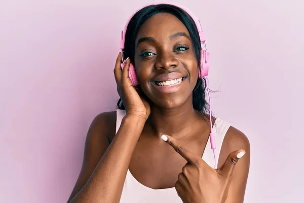 Mujer Afroamericana Joven Escuchando Música Usando Auriculares Sonriendo Feliz Señalando —  Fotos de Stock