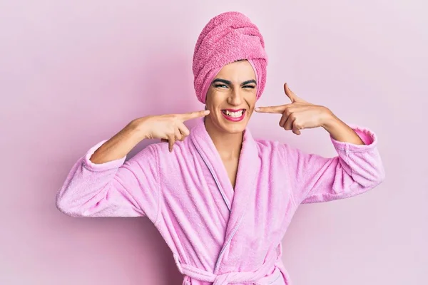 若い女性を身に着けている人は 頭の上にシャワータオルを身に着けて構成し バスローブは明るい表情と指の歯と口で指して笑っています 歯の健康の概念 — ストック写真