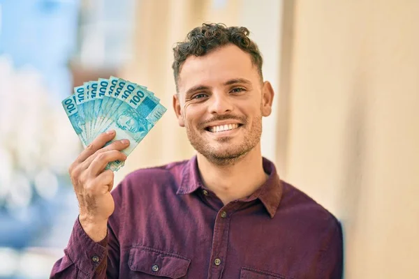 Joven Hispano Sonriendo Feliz Sosteniendo Billetes Reales Brasileños Ciudad —  Fotos de Stock