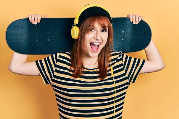 Redhead Young Woman Holding Skate Wearing Headphones Celebrating Crazy Amazed — Stock Photo, Image