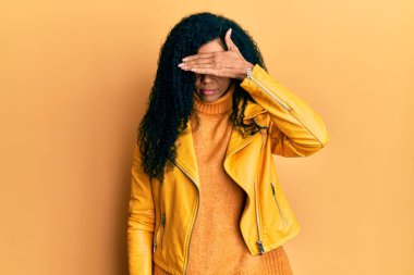 Orta yaşlı Afro-Amerikalı kadın yün kazak ve deri ceket giyip gözleri elle kaplayan, ciddi ve üzgün görünüyor. Görme, saklama ve reddetme konsepti 