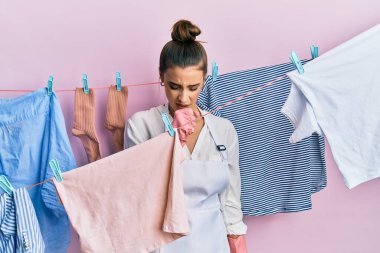 Güzel esmer bir kadın çamaşır ipinde çamaşır yıkıyor kendini iyi hissetmiyor ve soğuk algınlığı veya bronşitin belirtisi olarak öksürüyor. sağlık hizmeti kavramı. 