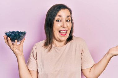 Orta yaşlı İspanyol kadın elinde yaban mersini tutarak başarıyı mutlu bir gülümsemeyle kutluyor ve kazanan el kaldırarak ifade ediyor. 