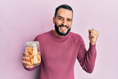 Sakallı genç adam elinde makarna kavanozuyla gururla bağırıyor, zaferi kutluyor ve kollarını kaldırarak çok heyecanlanıyor. 