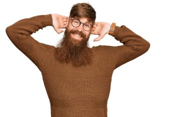 Genç İrlandalı kızıl elbiseli ve gözlüklü adam rahatlıyor ve esniyor, kolları ve elleri başının arkasında mutlu bir şekilde gülümsüyor. 