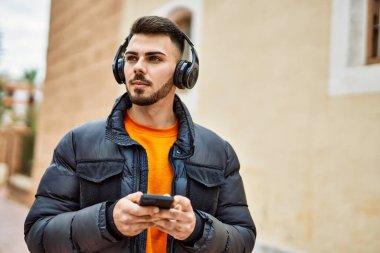 Yakışıklı, sakallı, mutlu ve kendine güvenen, akıllı telefon kullanan, kışlık palto giyen bir İspanyol.