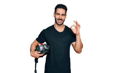 Sakallı, motosiklet kasklı İspanyol bir adam parmaklarıyla imza atıyor, gülümseyerek mükemmel bir sembol oluşturuyor. 