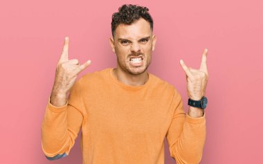 Latin asıllı genç adam, gündelik kıyafetler giyip çılgın bir ifadeyle bağırıyor ve elleri havada rock sembolü yapıyor. Müzik yıldızı. ağır kavram. 