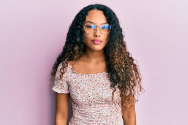 Yüzünde ciddi bir ifade olan günlük kıyafetler ve gözlük takan genç Latin bir kadın. Basit ve doğal bir şekilde kameraya bakıyorsun.. 