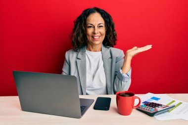 Ofiste çalışan orta yaşlı güzel bir kadın bir fincan kahve içiyor neşeli bir şekilde sunum yapıyor ve avuç içi kameraya bakıyor.. 