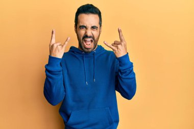 Latin asıllı genç adam, gündelik kıyafetler giyip çılgın bir ifadeyle bağırıyor ve elleri havada rock sembolü yapıyor. Müzik yıldızı. ağır kavram. 