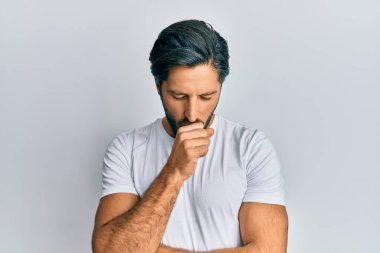 Günlük beyaz tişört giyen İspanyol genç adam kendini iyi hissetmiyor ve soğuk algınlığı veya bronşitin belirtisi olarak öksürüyor. sağlık hizmeti kavramı. 