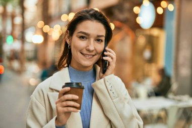 Genç İspanyol kadın akıllı telefondan konuşuyor ve şehirde kahve içiyor..