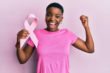 Genç Afrikalı Amerikalı kadın pembe kanser kurdelesi tutuyor gururla bağırıyor zaferi ve başarıyı kutluyor kollarını kaldırarak heyecanla 