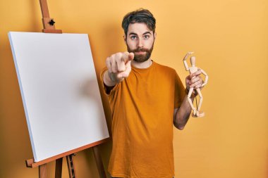 Boyacı sehpasında duran beyaz sakallı adam elinde manikinle kamerayı işaret ediyor. Kendine güvenen bir jest, ciddi görünüyor. 