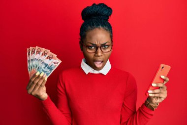 Amerikalı genç bir Afro-Amerikan kadını Avustralya dolarlarını elinde tutuyor. Şok olmuş, şüpheci ve alaycı görünüyor. 