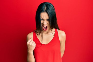 Kolsuz tişörtlü, sinirli ve kızgın genç İspanyol kız öfkeyle bağırırken sinirli ve öfkeli bir şekilde yumruk kaldırıyor. öfke ve agresif konsept. 