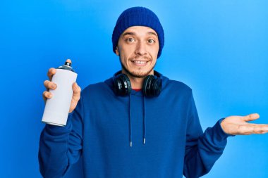 Süveter giyen İspanyol genç adam elinde grafiti spreyi ile başarıyı mutlu bir gülümsemeyle kutluyor ve kazanan el kaldırarak ifade ediyor. 