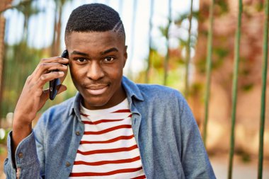 Genç Afrikalı Amerikalı gülümseyen mutlu bir adam şehirdeki akıllı telefondan konuşuyor..