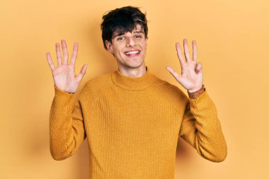 Yakışıklı hippi genç adam gündelik sarı süveter giyip dokuz numarayı gösterip gülümserken kendinden emin ve mutlu.. 