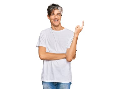 Gündelik beyaz tişört giyen genç İspanyol adam gülümsüyor mutlu bir şekilde elini ve parmağını yana doğru gösteriyor. 