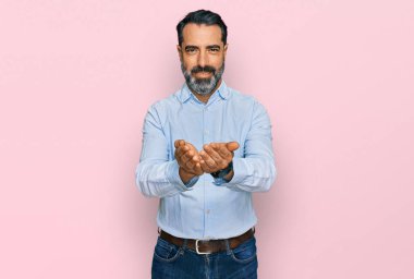 Orta yaşlı, sakallı, iş gömleği giyen, elleri avuçlarında gülümseyen, el hareketi yapan bir adam. Bekleme ve koruma 