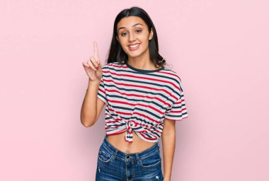 Gündelik giysiler giyen genç İspanyol kız bir numarayı gösterip işaret ederken kendinden emin ve mutlu bir şekilde gülümsüyor.. 
