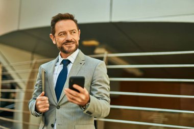 Şehirdeki akıllı telefondan gülümseyen orta yaşlı bir işadamı..