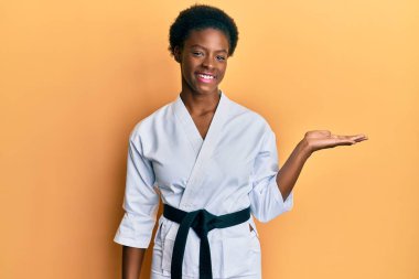 Genç Afrikalı Amerikalı kız karate kimonosu ve siyah kuşak takmış neşeli bir şekilde gülümsüyor ve avuç içi kameraya bakıyor.. 