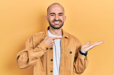 Sıradan kıyafetler giyen genç kel adam kameraya hayret ediyor ve gülümsüyor.. 