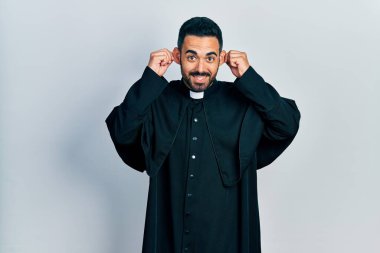 Sakallı, Katolik rahip cüppeli, kulakları parmaklarıyla çeken yakışıklı bir İspanyol. Komik bir jest. deneme sorunu 