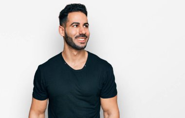 Sakallı, sıradan siyah tişörtlü, yüzünde gülümsemeyle yan yana bakan İspanyol bir adam. Kendinden emin gülen. 