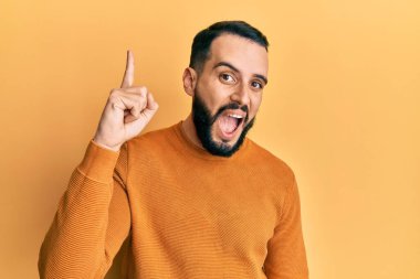 Kış süveteri giyen sakallı genç adam başarılı bir fikri işaret ediyor. Heyecanlı ve mutlu. Bir numara.. 