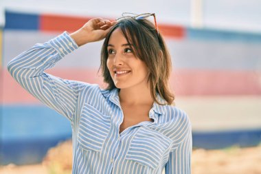 Genç İspanyol kadın gülümsüyor, şehirde güneş gözlüklerine dokunduğu için mutlu..