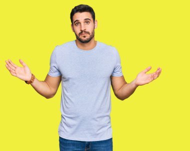 Sıradan kıyafetler giyen, elleri ve kolları havada, kafası karışmış genç İspanyol bir adam. şüphe kavramı. 