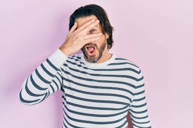 Orta yaşlı beyaz bir adam, günlük kıyafetler giymiş, şok içinde yüzünü ve gözlerini kapatarak utanmış ifadesiyle parmaklarının arasından bakıyor.. 