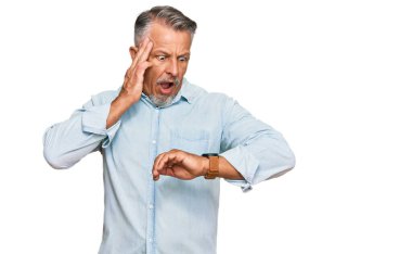 Orta yaşlı, gri saçlı, günlük kıyafetler giyen, saati izleyen, geç kalmaktan korkan bir adam. 