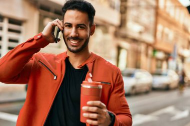 Genç İspanyol adam akıllı telefondan konuşuyor. Şehirde kahve içiyor..