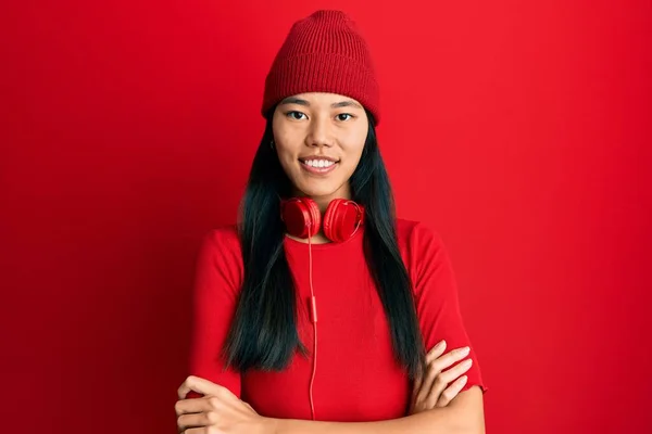 Young chinese woman listening to music using headphones happy face smiling with crossed arms looking at the camera. positive person.